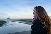 Frankreich, Manche, der Mont-Saint-Michel, junge Frau betrachtet die Insel und die Abtei bei Sonnenaufgang von der Mündung des Couesnon