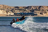 Morocco, Western Sahara, Dakhla, fishermen taking the sea on their boat in front of the beach of Araiche bordered by a cliff