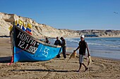 Marokko, Westsahara, Dakhla, Fischer entladen Fisch in der Nähe ihres blauen Bootes am Strand von Araiche, der von einer Klippe begrenzt wird