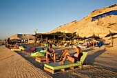 Marokko, Westsahara, Dakhla, Kitesurfer auf Liegestühlen vor der Kitecamp-Bar Dakhla Attitude bei Sonnenuntergang