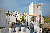 Marokko, Tanger Region Tetouan, Tanger, Marokkanische Frauen auf der Terrasse des Hotels Abyssinian in Tanger, mit Blick auf einen weißen zinnenbewehrten Turm mit Blick auf das Mittelmeer