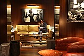 Frankreich, Paris, Hotel Royal Monceau, Mann sitzt auf einem Ledersofa und zündet sich eine Zigarre an im Vinales, dem privaten Zigarrenclub des Royal Monceau