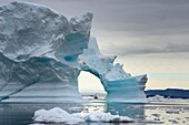 Greenland, North West Coast, Baffin Sea, Inglefield Fjord towards Qaanaaq, iceberg forming an arch and an exploration PolarCirkel boat (zodiac) of the MS Fram cruse ship from Hurtigruten