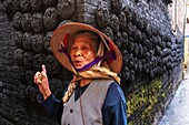 Vietnam, Bat Trang, in der Nähe von Hanoi, Keramikerdorf, lächelnde Frau vor Kohleklumpen, die an einer Wand eines traditionellen Hauses kleben