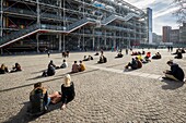 France, Paris, Les Halles district, tourists sitting on the forecourt of the Pompidou Center or Beaubourg, architects Renzo Piano, Richard Rogers and Gianfranco Franchini