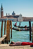 Italy, Veneto, Venice listed as World Heritage by UNESCO, a man lounging on the banks of the Grand Canal and in front of the Basilica and Abbey San Giorgio Maggiore