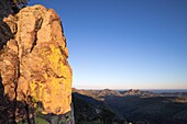 Frankreich, Var, Frejus, Esterel-Massiv, rotes Rhyolithgestein vulkanischen Ursprungs mit gelben Flechten bedeckt, im Hintergrund die Gipfel des Cape Roux Peak