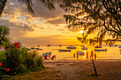 Blick auf Boote und Menschen am öffentlichen Strand von Mon Choisy bei Sonnenuntergang, Mauritius, Indischer Ozean, Afrika