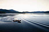 USA, New York, Lake Placid, Man in wooden boat on lake at sunrise