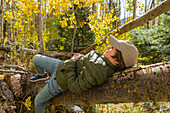 USA, New Mexico, Lächelnder Junge liegt auf einem Baumstamm im Santa Fe National Forest