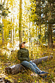 USA, New Mexico, Nachdenklicher Junge sitzt auf einem Baumstamm im Santa Fe National Forest