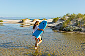 Südafrika, Hermanus, Teenager-Mädchen geht am Strand mit Bodyboard spazieren