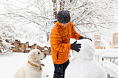 Junge mit seinem Hund baut Schneemann
