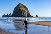 USA, Oregon, Rückansicht einer Frau, die in der Nähe des Haystack Rock in Cannon Beach spazieren geht