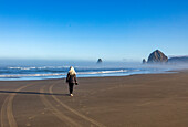 USA, Oregon, Rückansicht einer Frau bei einem Spaziergang in der Nähe des Haystack Rock in Cannon Beach im Morgennebel