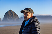 USA, Oregon, Man standing near Haystack Rock at Cannon Beach in morning mist