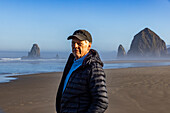 USA, Oregon, Portrait of man standing near Haystack Rock at Cannon Beach in morning mist