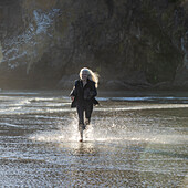 USA, Oregon, Newport, Woman running on sandy beach and splashing water 