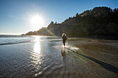 USA, Oregon, Newport, Frau läuft am Sandstrand und spritzt Wasser