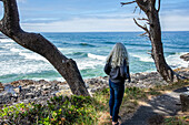Senior woman looks out to sea on rocky headland 