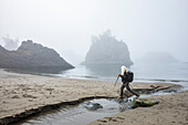 USA, Oregon, Brookings, Senior woman hiking with nordic walking poles on beach