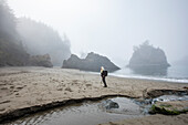 USA, Oregon, Brookings, Ältere Frau steht am Strand in der Nähe eines Baches