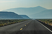 Leerer Highway, der durch die Wüste führt, mit Bergen im Hintergrund