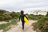 Boy (10-11) walking towards beach with body board