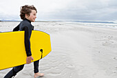 Junge (10-11), der am Strand läuft und ein Bodyboard trägt