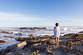 South Africa, Hermanus, Boy (10-11) standing on rocks on Kammabaai Beach