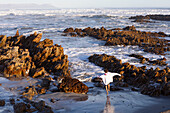 Südafrika, Hermanus, Junge (10-11) läuft zwischen Felsen am Kammabaai Beach