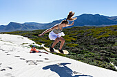 South Africa, Teenage girl (16-17) and boy (10-11) sand boarding in Walker Bay Nature Reserve