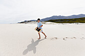 Boy (10-11) carrying surfboard in Walker Bay Nature Reserve