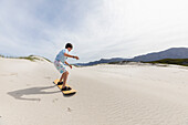 Junge (10-11) beim Sandboarden im Walker Bay Naturreservat