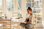 Teenage girl (16-17) playing guitar in dining room