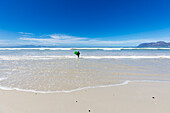 Junge (10-11) mit Surfbrett läuft auf leerem Strand