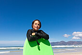 Boy (10-11) with surfboard posing on Muizenberg Beach