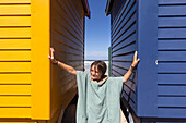 Boy (10-11) posing in front of colorful beach hut on Muizenberg Beach