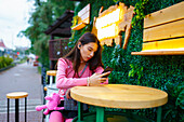 Junge Frau mit Smartphone sitzt in einem Straßencafé