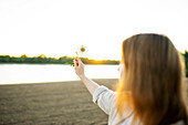 Woman holding chamomile flower on beach at sunset