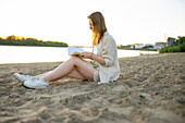 Frau liest Buch am Strand bei Sonnenuntergang