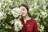 Junge Frau steht mit geschlossenen Augen an einem blühenden Baum
