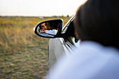 Reflexion einer jungen Frau im Seitenspiegel eines Autos