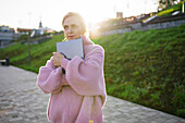 Woman embracing laptop while standing outdoors at sunrise