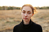 Portrait of serious woman standing in field at sunset