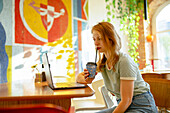 Side view of woman working on laptop while drinking coffee in cafe 
