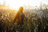 Junge Frau, die in der Morgendämmerung auf einem Feld spazieren geht