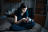 Ernste Frau, die auf dem Bett sitzend ein Smartphone benutzt