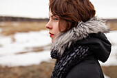 Porträt einer nachdenklichen Frau mit Blick auf ein Feld in einer Winterlandschaft