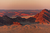 Licht beleuchtet die Naukluft-Berge und die Namib-Wüste bei Sonnenaufgang. Namib-Naukluft-Park, Namibia.